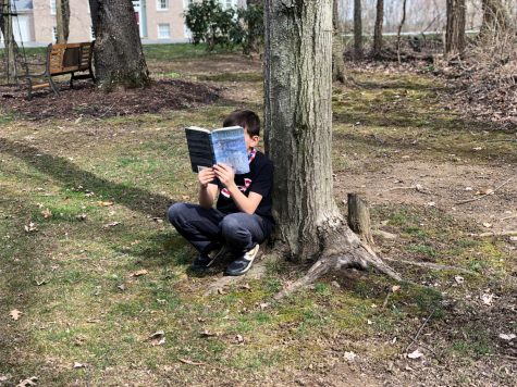 Xavier Garland, fifth grader, reads a book underneath a tree in the warm spring light.

