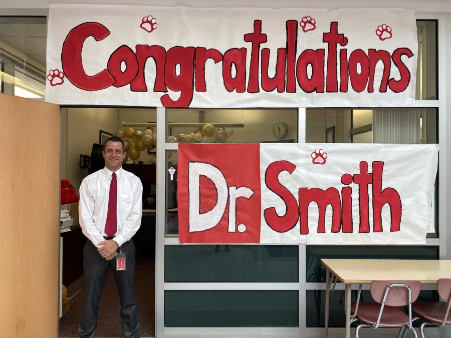 Dr. Smith poses with a sign in front of his office celebrating his doctoral success.