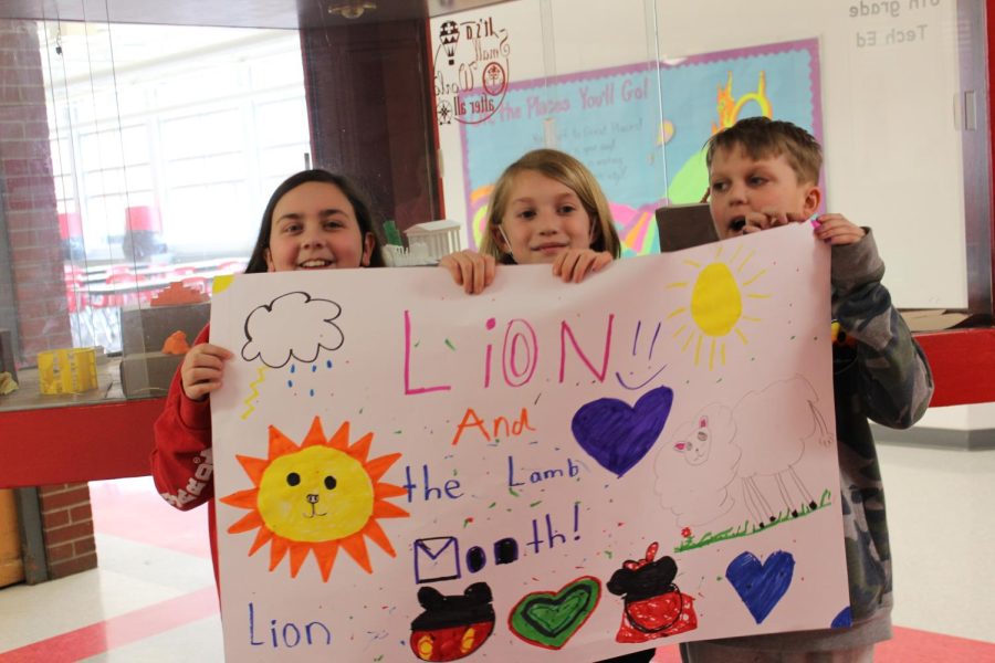Students Abby Tedesco, Shane McGowan, and Kate VanDeCar are holding a sign for Lion and the Lamb month.