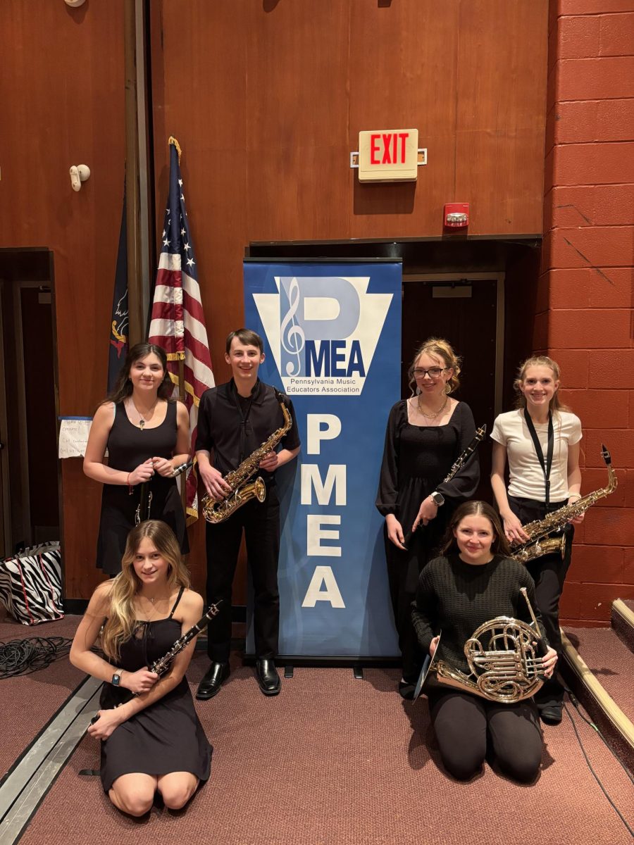 Klaire Evans (8), Emme Borrelli (8), Lincoln Murphy (8), Hailey Scenock (9), Madison Capehart (9), and Katelyn VanDeCar (9) attend District Band. They pose for a group photo in front of the PMEA sign.